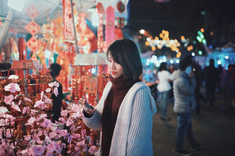 Young woman touching flowers in market at night