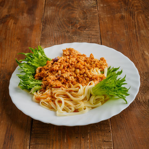 A plate of pasta in bolognese sauce on a wooden table. vertical photo