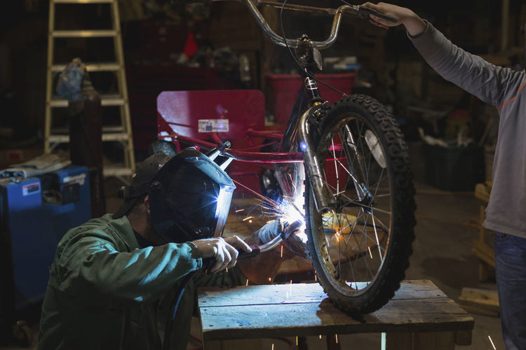 Father and son welding tricycle while working in workshop