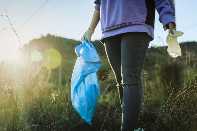 Volunteer walking in grass holding garbage bag on sunset