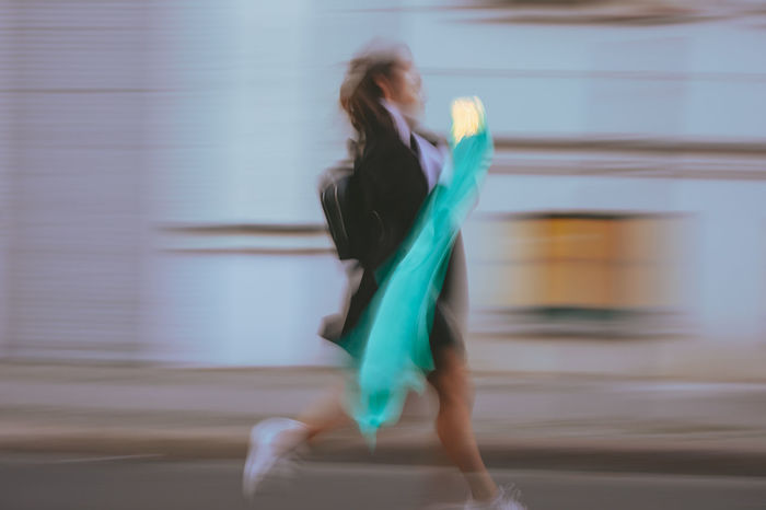 Side view of woman holding illuminated lighting equipment with scarf running on road in city
