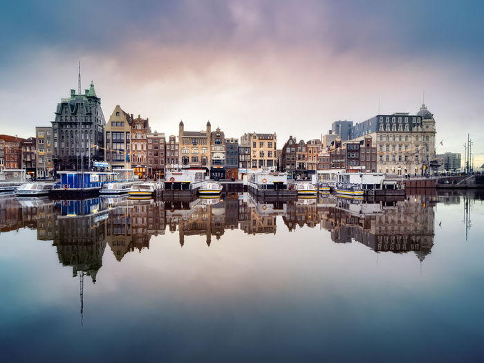 Reflection of historic canal houses and tourist canal boats in the damrak canal in amsterdam.