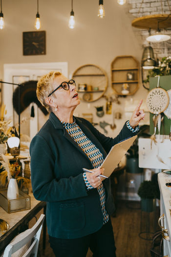 Senior female owner holding clipboard while doing inventory at decor shop