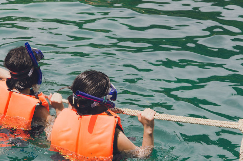 Rear view of people holding rope while snorkeling in sea
