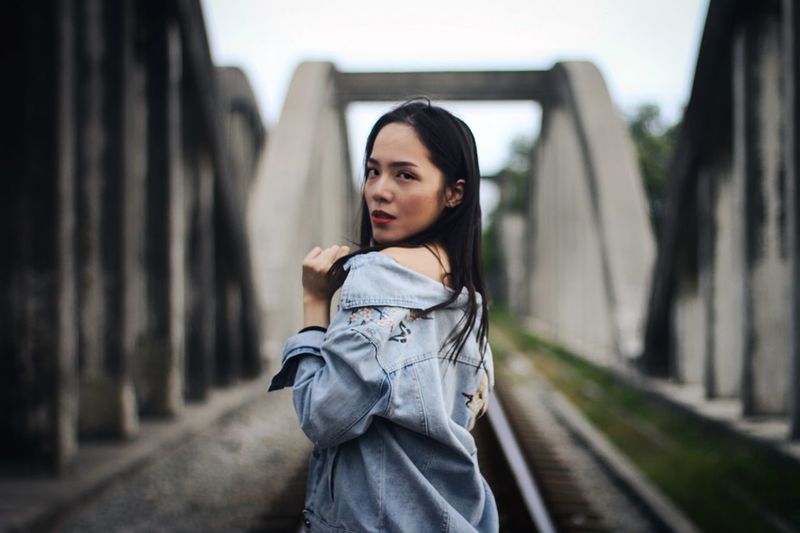 Portrait of beautiful young woman standing at railroad bridge
