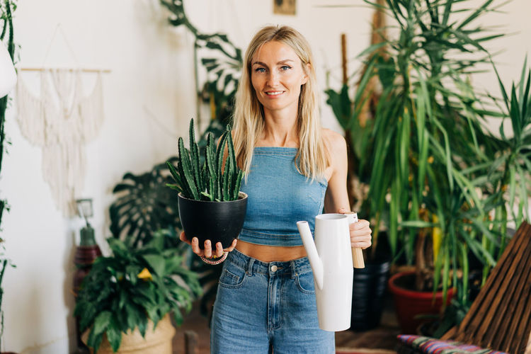 Woman in home greenhouse with potted plant and watering can.
