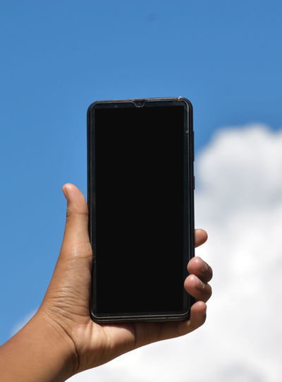 Close-up of person holding smart phone against sky