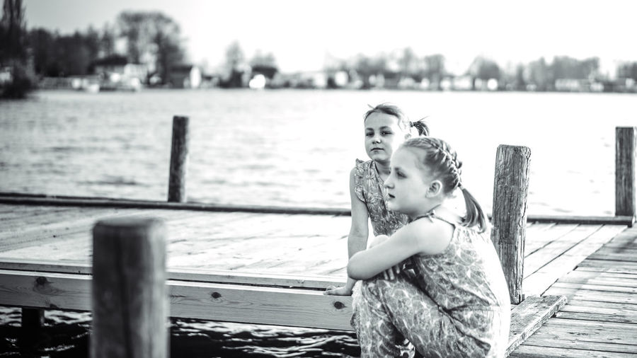 Siblings sitting on pier over lake against sky