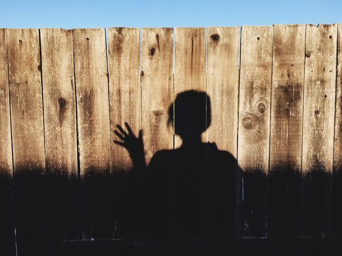 Shadow of person gesturing in front of wooden fence