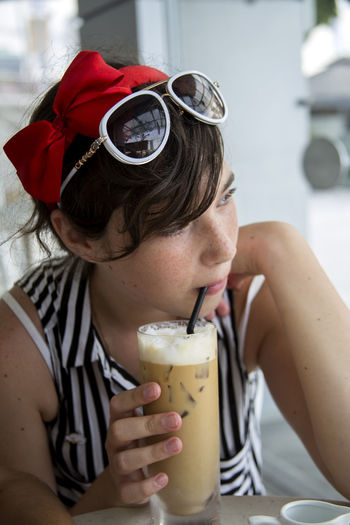 Thoughtful woman looking away while drinking iced coffee at cafe