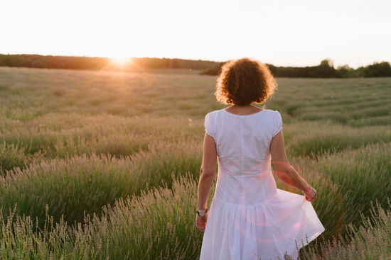 Rear view of woman standing on field against sky during sunset