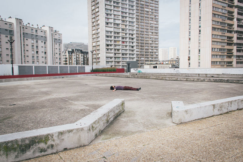 Young man lying on land against buildings in city
