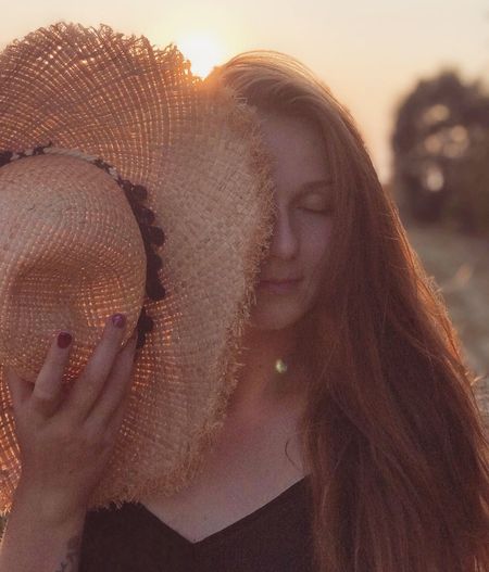 Close-up portrait of young woman in hat during sunset