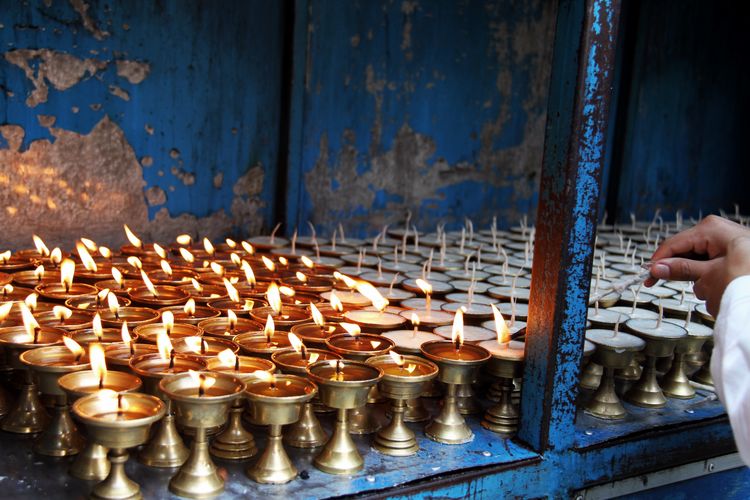 Midsection of person holding candles burning in temple