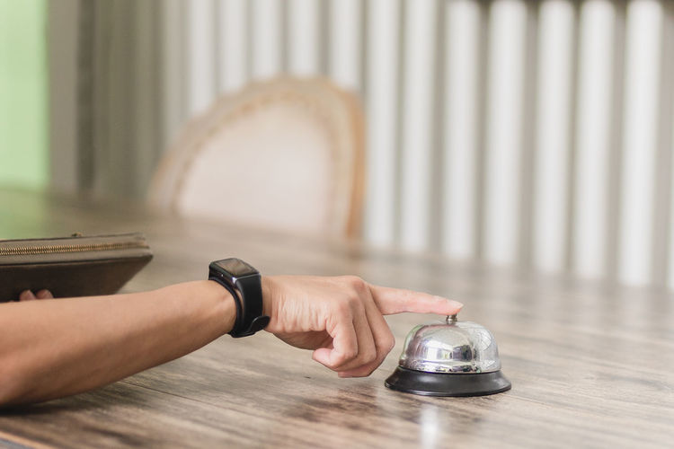 Woman hand pressing a hotel service bell at reception counter.