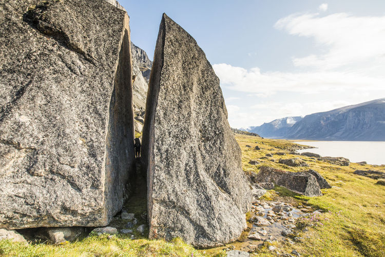 Backpacker squeezes through cracked erratic rock in the arctic.