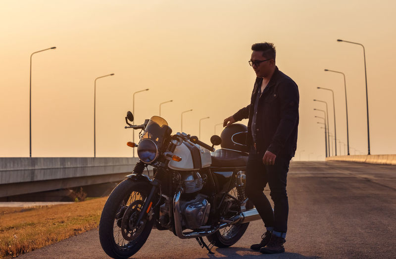 Summer travel on a motorcycle, motorcycle driver in black leather jacket stands on road with vintage 