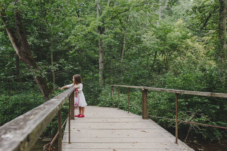 Full length of carefree girl standing on wooden footbridge at forest