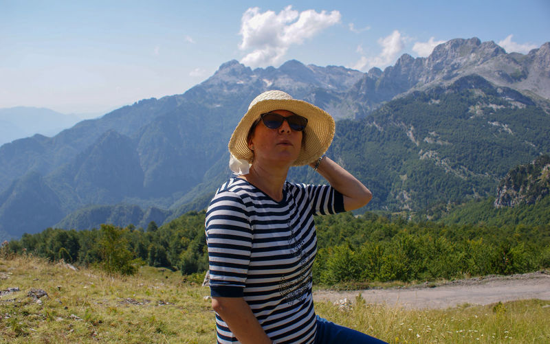 Woman wearing sunglasses and hat sitting against mountain