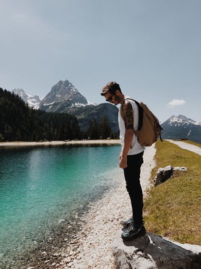 Full length of young man standing by lake against mountains