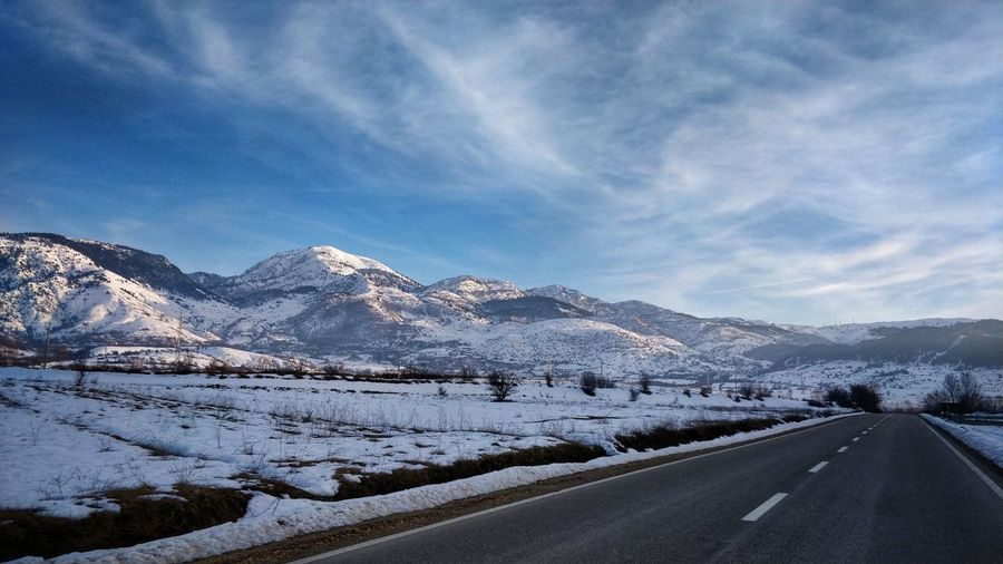 Road by snowcapped mountains against sky