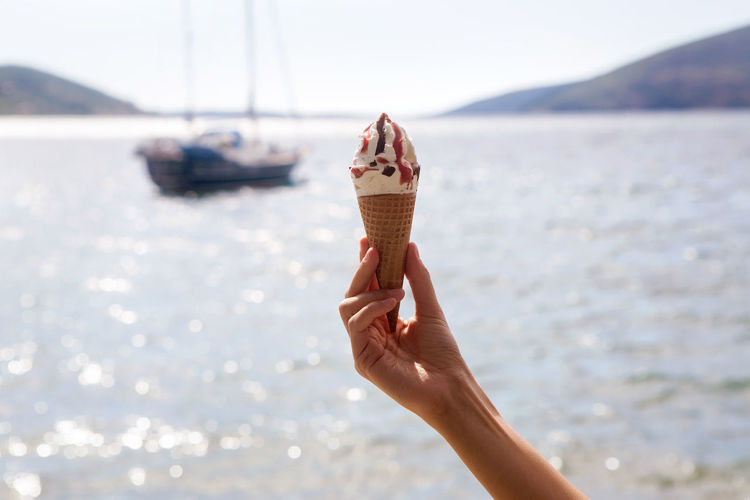 Ice cream cones with chocolate and jam in a female hand on a background of sea and yachts