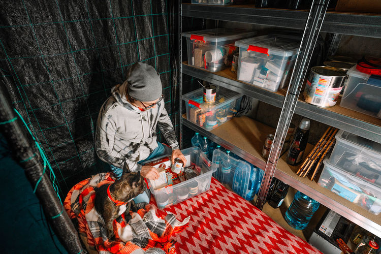 Man and french bulldog checking survival food supplies in underground emergency shelter