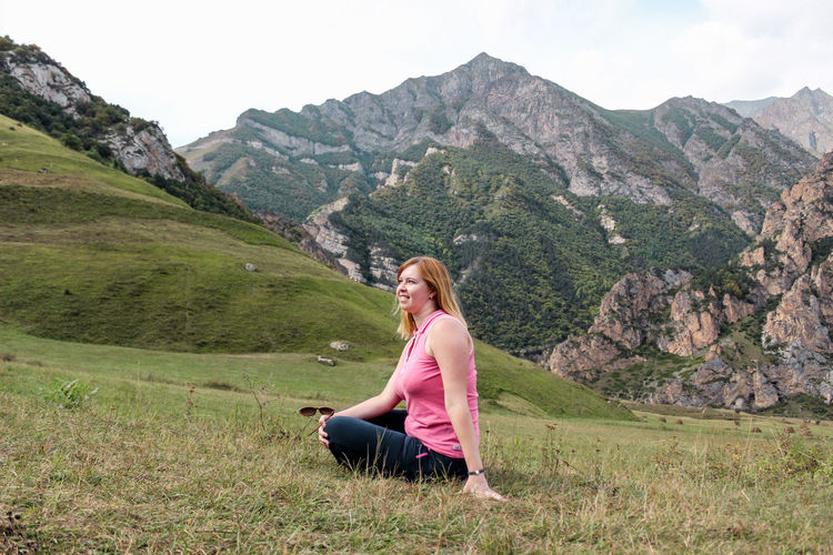 Side view of young woman sitting on field against mountain