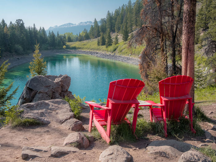 Red chairs on shore by lake against trees