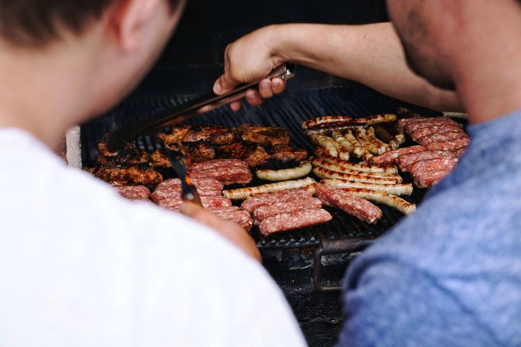 Midsection of men preparing food on barbecue grill