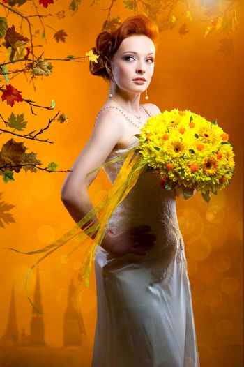 Beautiful bride holding bouquet while standing against orange background