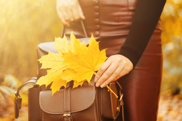 Midsection of woman holding yellow umbrella standing during autumn