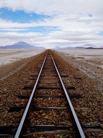 Railroad track leading mountains against sky