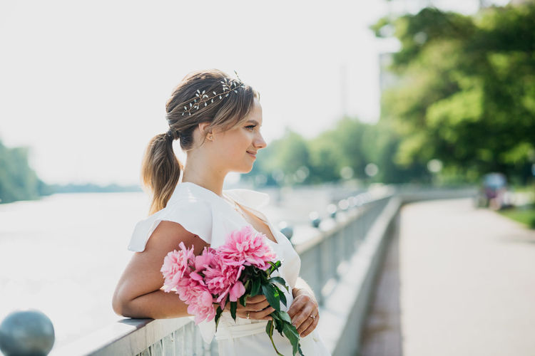 Side view of woman holding flowers standing by railing