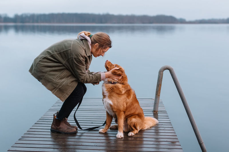 side view of man with dog on pier against lake