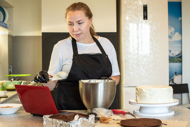 Blogger pastry chef cook confectioner  makes a cake. woman in apron using notebook while cooking.