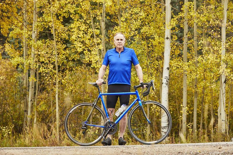 Full length portrait of senior man with bicycle standing against trees