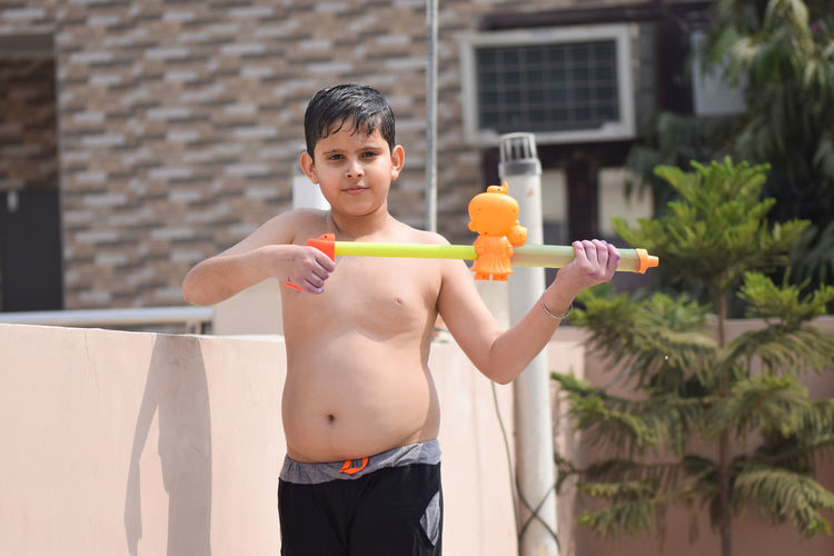 Portrait of shirtless boy playing with squirt gun during holi