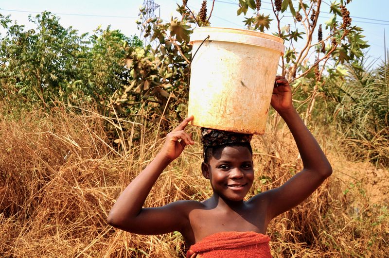 Portrait of smiling young woman carrying bucket on head in forest