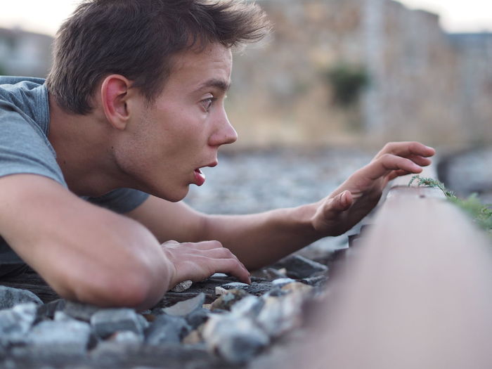 Close-up of surprised young man touching moss while lying on field