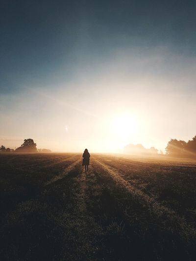 Scenic view of woman walking on empty field at sunrise