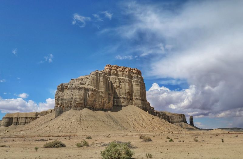 Landscape of large multi tiered butte, rock formation, sand and bright clouds in utah