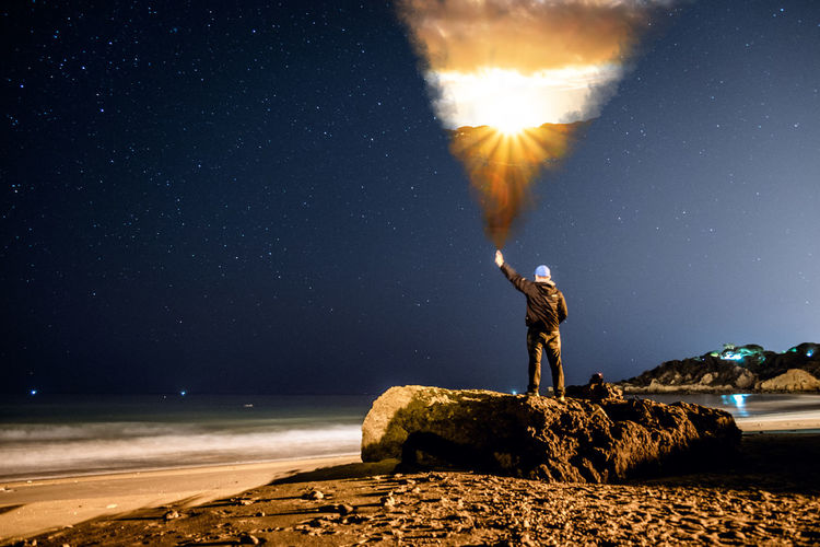 Man standing on rock at beach against sky at night