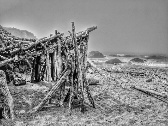 Driftwood structure against foggy ocean and sandy beach.