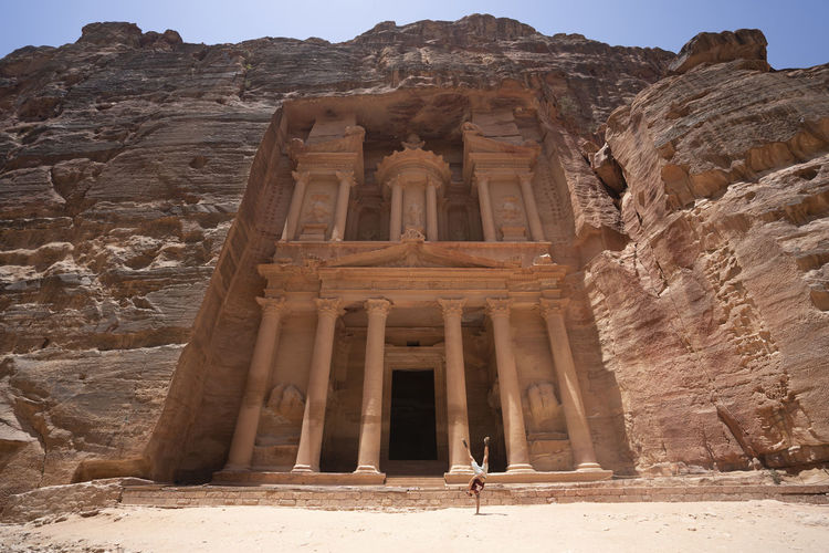 A man does a hand stand near treasury monument in petra, jordan seven wonders