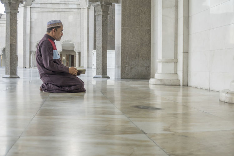 Side view of mature man reading koran while kneeling at mosque