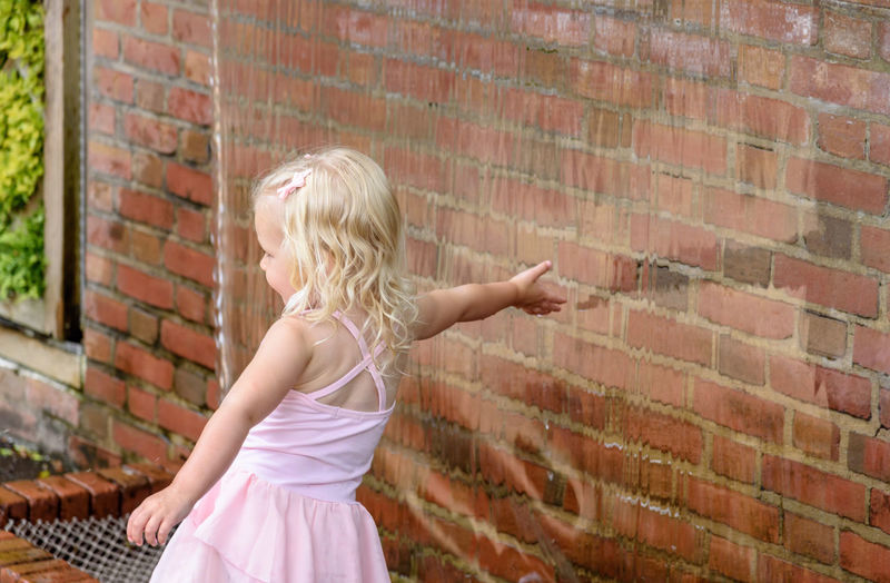 Rear view of girl touching artificial waterfall over brick wall