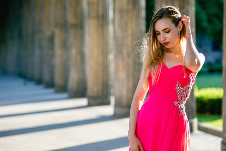 Beautiful young woman in pink evening dress standing at colonnade
