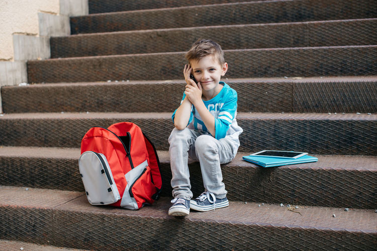 Full length of boy talking on mobile phone while sitting on steps