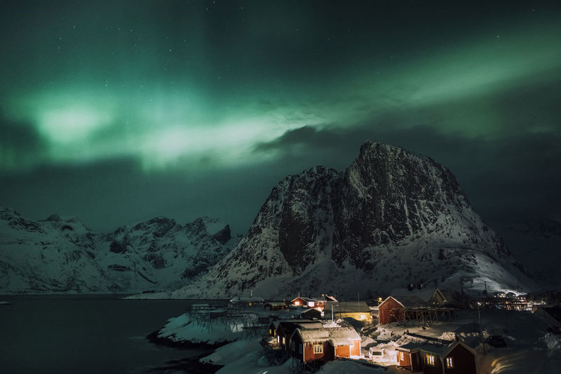 Scenic view of sea by snowcapped mountains against sky at night